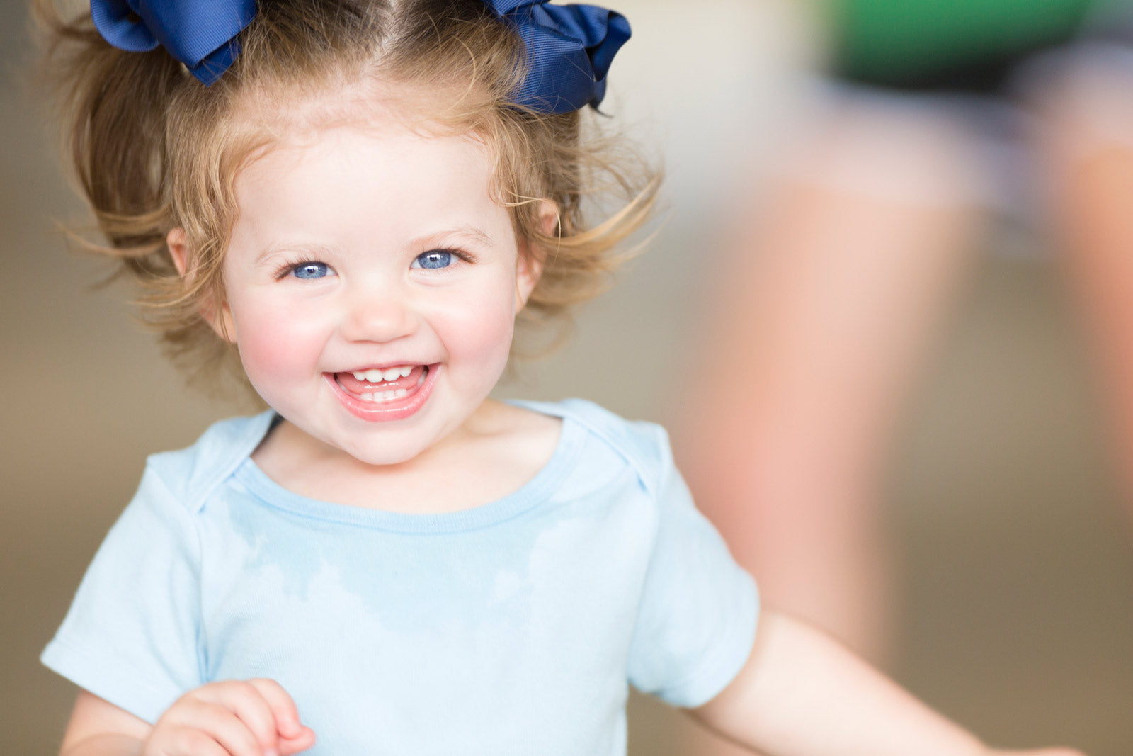 A toddler girl wearing blue bows in her hair with a blue romper on