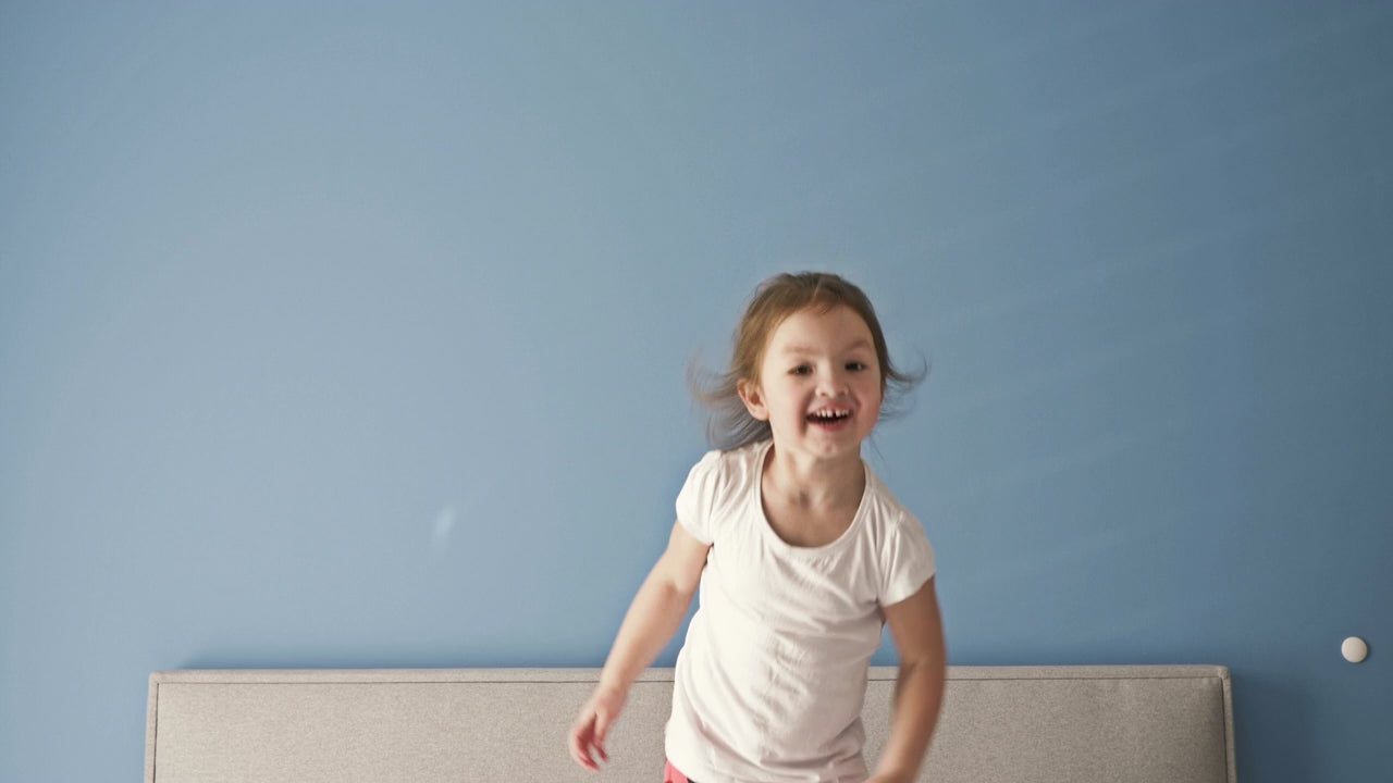 A toddler girl jumping joyfully on her parent's bed.